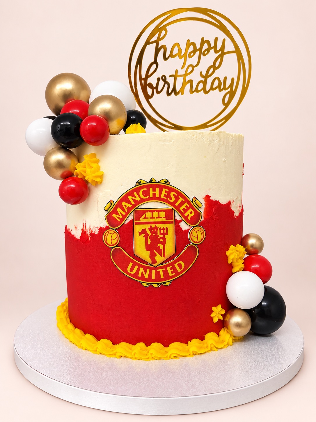 Red and cream Manchester United themed cake with the club crest, red, black and gold balls and a Happy Birthday topper