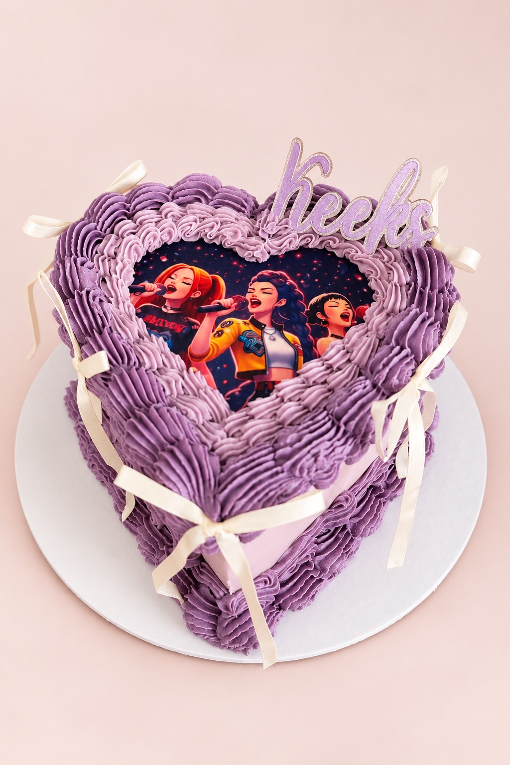 Purple heart-shaped vintage cake with frilly piping, cream ribbon bows, an edible cartoon picture and a lilac name topper